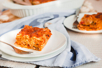 Slice of delicious beef lasagne with cheese crust on a white plate viewed close up on the side showing the layers.Restaurant menu, recipe