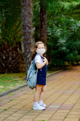 a little girl, a schoolgirl, goes to school on the street with a denim backpack, and in a medical mask