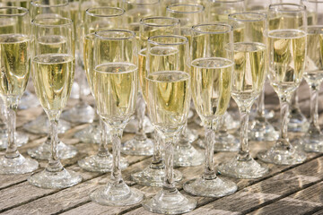 Arrangement of filled champagne glasses in the sunlight at outdoor wedding