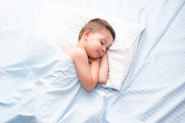 Cute four five year old toddler boy sleeping calm on fresh blue bedding with white pillow.
