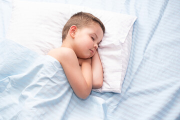 Cute four five year old toddler boy sleeping calm on fresh blue bedding with white pillow.