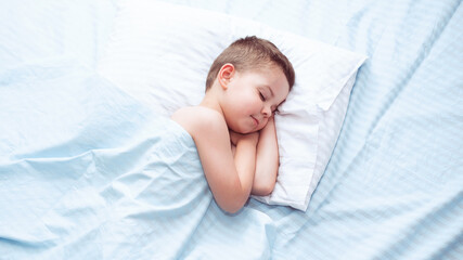 Cute four five year old toddler boy sleeping calm on fresh blue bedding with white pillow.