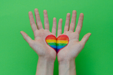 Open hands with rainbow LGBT heart over green background. LGBTQ right concept. LGBT equality symbols.
