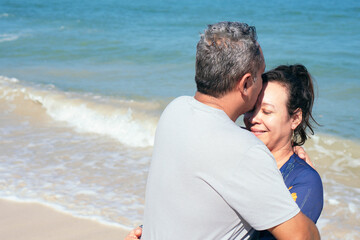 Mature Hispanic couple cuddling standing on the beach Mature couple cuddling standing on the beach