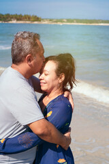 Fototapeta na wymiar Mature couple cuddling and hugging sitting at the beach during morning time