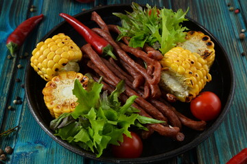 chorizo, sausages with grill corn and salad with food ingredients on rustick wooden table closeup