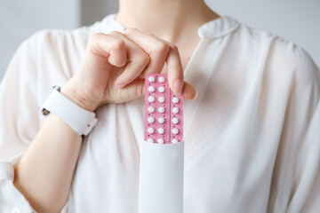 Unrecognized woman in white blouse holding hormonal oral contraceptives in a pink blister. Concept...