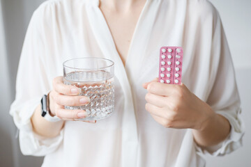 Unrecognized woman in white blouse holding hormonal oral contraceptives in a pink blister. Concept of Hormonal methods of birth control. Estrogen and Progestin hormonal balance.