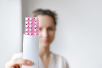 Unrecognized woman in white blouse holding hormonal oral contraceptives in a pink blister. Concept...