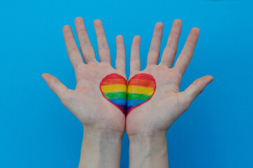 Female hands with a rainbow LGBT flag painted in her palms on a blue background. LGBTQ community sign. LGBT rights equality concept.