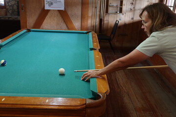 Woman Playing Pool in a Recreational Clubhouse ready to hit the Cue ball and Send another Ball into the Side Pocket