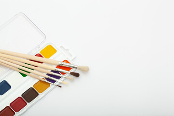 A set of watercolor paints and paint brushes on a white background with a copy space for text