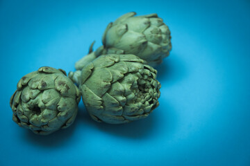 Obraz premium Image of three raw artichokes on a blue background with copy space