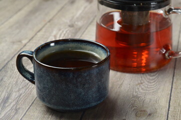 cup of black tea on wooden table, with glass teapot blurred background.