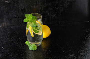 A large glass of water with lemon, mint leaves. A glass of lemonade on a black textured background.