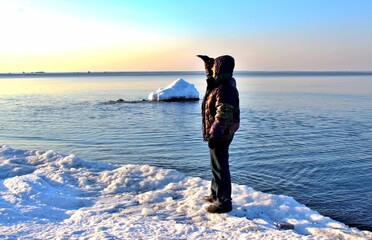 A man standing on an ice floe in the sea and looking into the distance