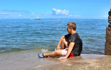 Boy sitting by the sea and looking into the distance