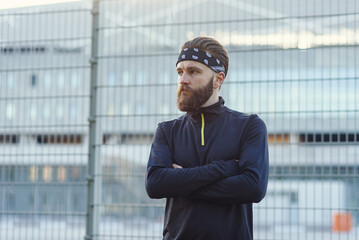 Male bearded athlete in sports uniform and bandana after hard training on the playground.