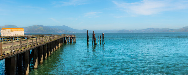 Old wooden pier and beautiful turquoise ocean water panoramic sea and harbor landscape background. Clear blue seashore in San Francisco Bay 