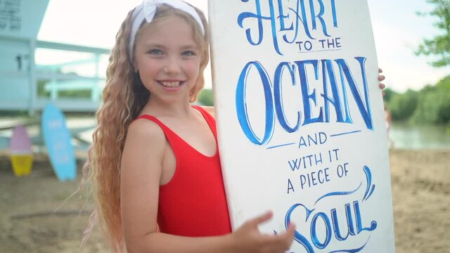 Young pretty blond girl in red bikini posing with surfboards against blue lifeguard tower on the sand beach.