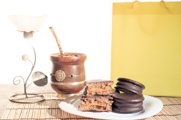 Alfajores Argentinos de chocolate y dulce de leche acompañado de mate y café, en fondo rojo, amarillo y negro