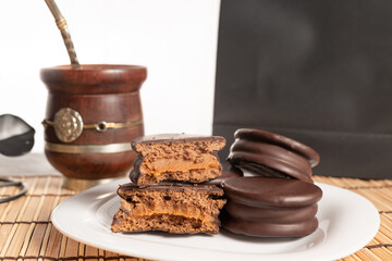 Alfajores Argentinos de chocolate y dulce de leche acompañado de mate y café, en fondo rojo, amarillo y negro