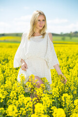 Naklejka na ściany i meble Young female posing in yellow oilseed rape field wearing in white dress outdoor