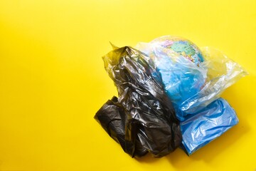 Globe wrapped in a plastic blue and black bags on a yellow background. Creative concept. Plastic free. Ban plastic pollution. Flat lay. Copy space.