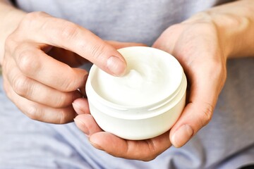 Girl is holding a jar of cosmetic cream in her hands. Skin care, minimalist. Preserve youthfulness and elasticity of the skin. Selective focus.