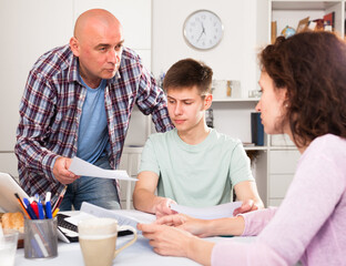 Parents with teenager son using laptop and analyzing their finances with documents at table