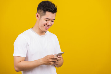 Asian handsome young man smiling positive using smartphone to get in touch screen or typing message, male reading good news message enjoy mobile application, studio shot isolated on yellow background