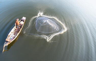 Asian fisherman on wooden boat casting a net for catching freshwater fish in nature river in the...