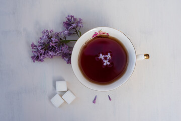 A cup of tea with sugar on a white background and a branch of lilac.