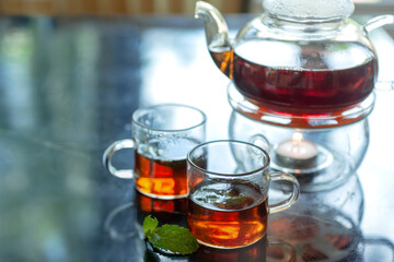 Hot black tea with fresh mint leaves, transparent cup of tea and teapot, closeup photo