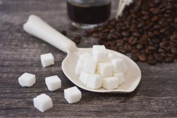 Cube sugar on the ladle with roasted coffee beans background. These are the nutritive sweeteners. sucrose or table sugar made of fructose and glucose from the cane. 