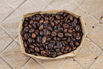Coffee beans in a brown paper bag on wooden background.