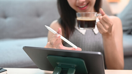 Cropped shot woman drinking coffee and reading news on digital tablet at home.