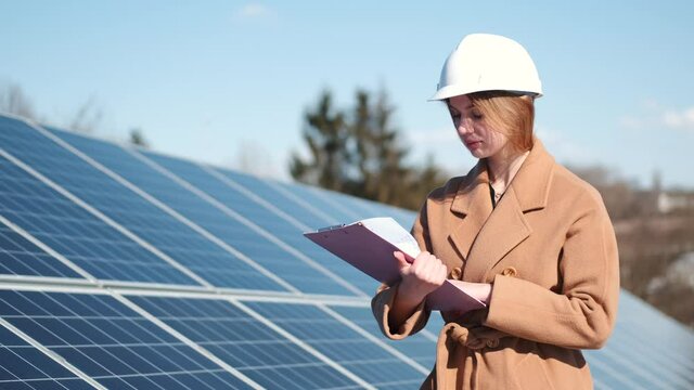 Young woman with checklist standing at solar plant
