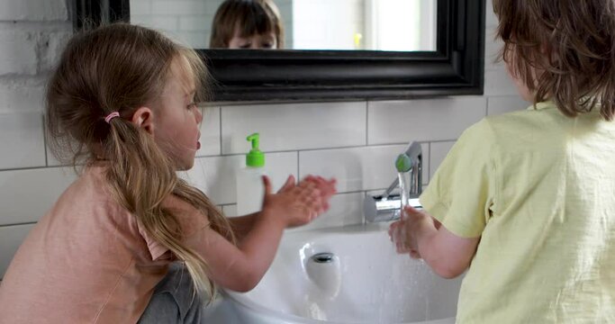 Funny kids preschoolers girl and boy wash hands and take soap at white sink by mirror in bathroom at home close backside view
