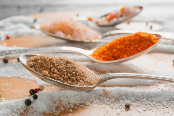 Spoons with different salt and peppercorns on table, closeup