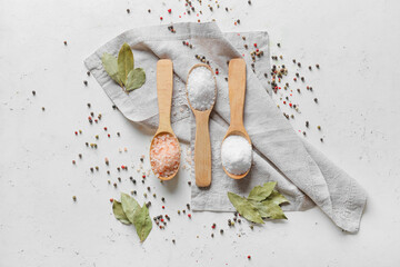 Spoons with different salt, bay leaves and peppercorns on light background