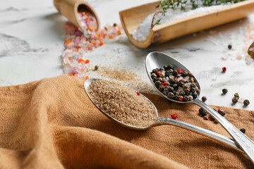 Spoons with different salt and peppercorns on light background, closeup