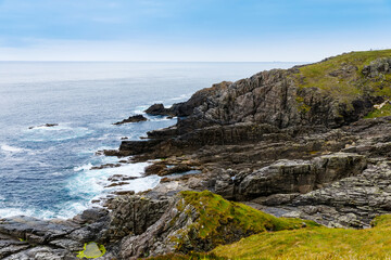 Fototapeta na wymiar Rugged landscape at Malin Head, County Donegal, Ireland. Rough beach with cliffs, green rocky land with sheep on foggy cloudy day.