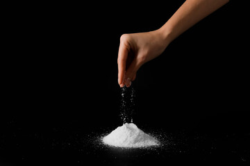 Woman sprinkling salt on dark background, closeup