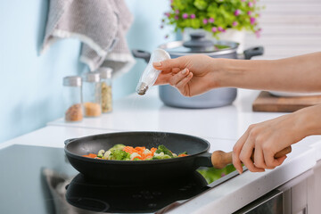 Woman preparing vegetables on electric stove in kitchen