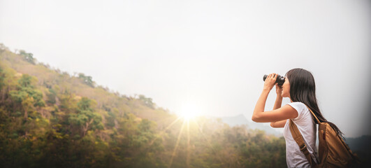 Tourist asia woman backpacking travel adventure in the forest and use binocular looking on top of...