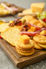 Board with tasty crackers with cheese and snacks on grey background