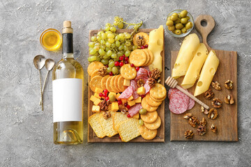 Obraz na płótnie Canvas Board with tasty crackers with cheese, bottle of wine and snacks on grey background