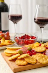 Board with tasty crackers with cheese, glasses of wine and snacks on table