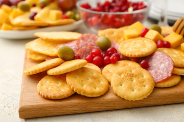 Board with tasty crackers with cheese and snacks on light background